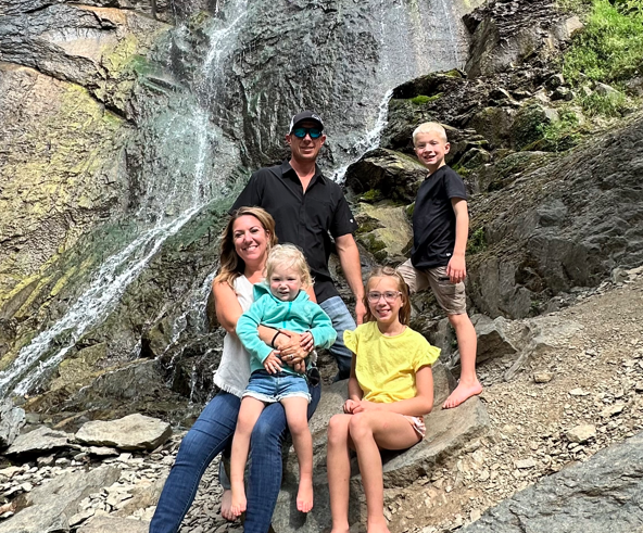 Family posing on rocks by a waterfall, with children and adults smiling outdoors