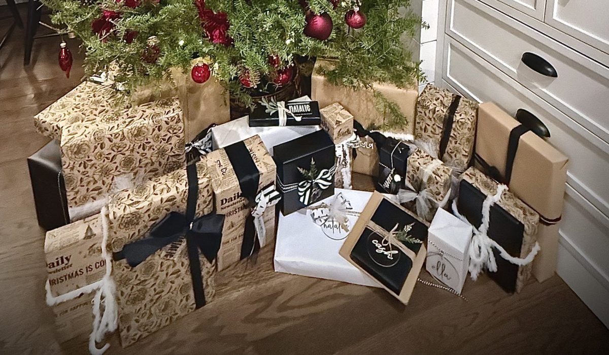 Wrapped Christmas gifts under a decorated tree on a wooden floor near a dresser.