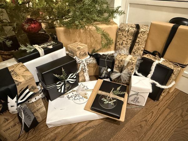 Wrapped gifts in black, white, and gold under a decorated Christmas tree on a wooden floor