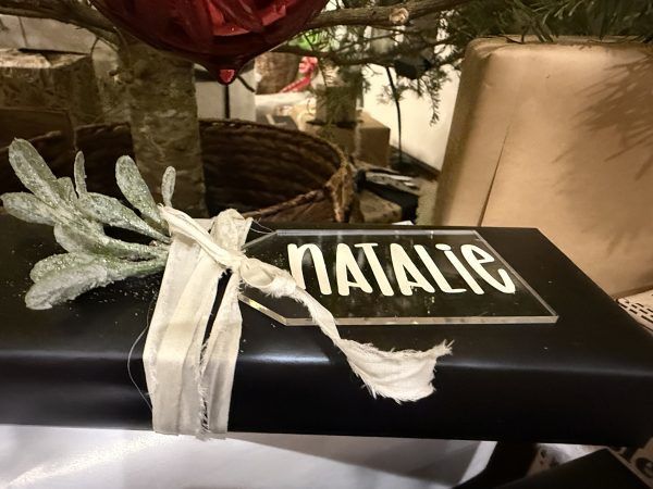 Black gift box tied with a white ribbon and silver leaf decoration, labeled “NATALIE”