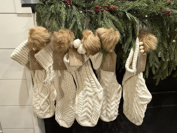 Five cream knit Christmas stockings hanging from a garland on a mantel