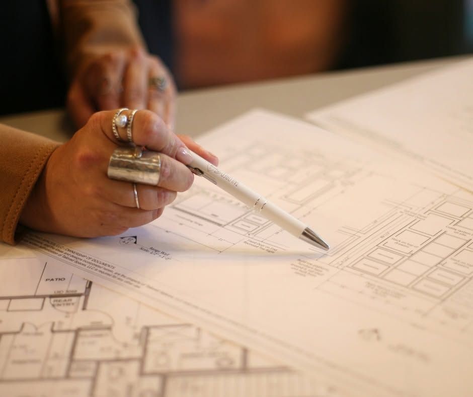 Hand holding a pen over architectural blueprints on a desk