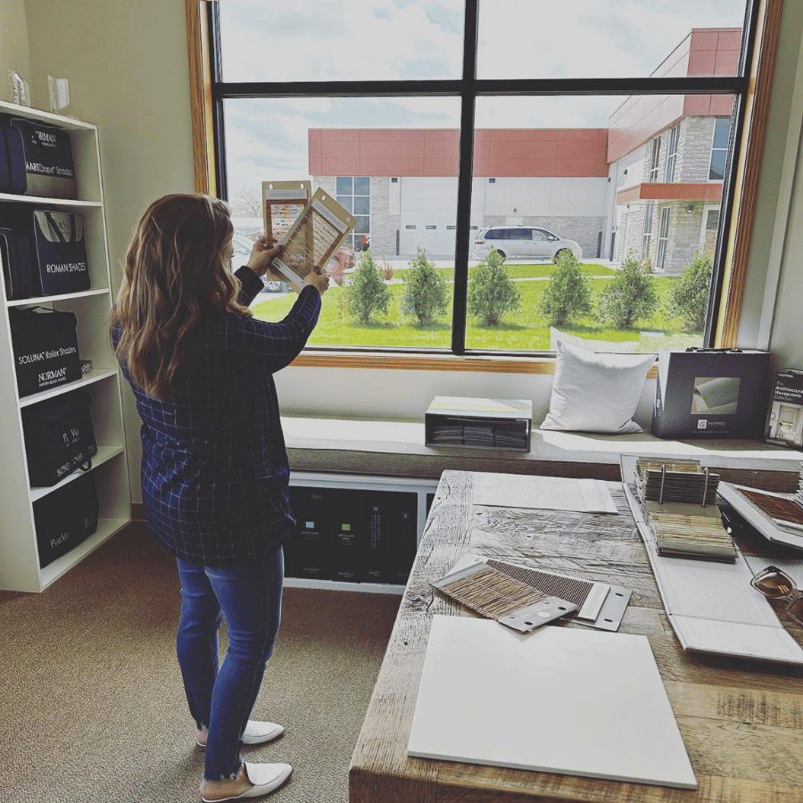 Person holding up a framed sample in a bright showroom with large windows and display tables