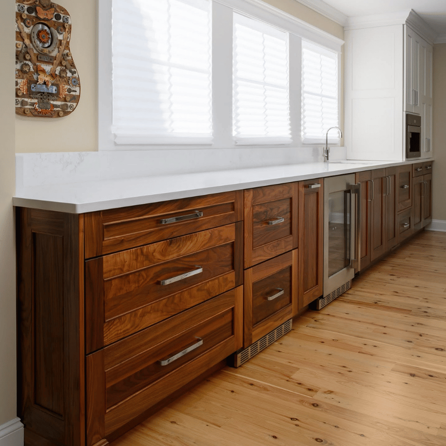 Long wooden kitchen island with white countertop, sink, and white window blinds in a bright room