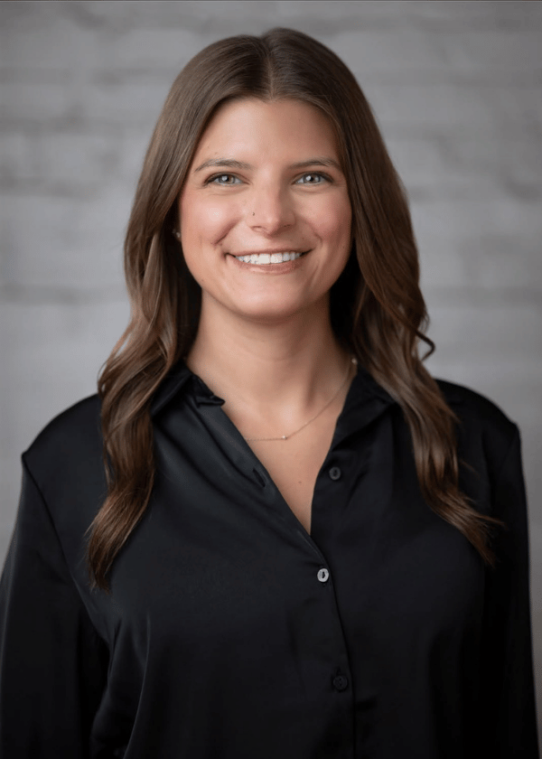 Portrait of a smiling woman in a black blouse against a gray studio background