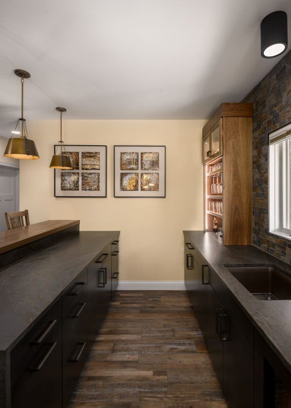 Modern kitchen or bar area with dark counters, wood floors, pendant lights, and framed wall art