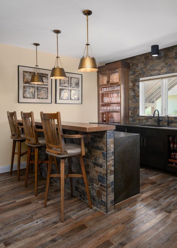 Rustic kitchen with wood bar stools, pendant lights, stone accents, and a dining table by a window.
