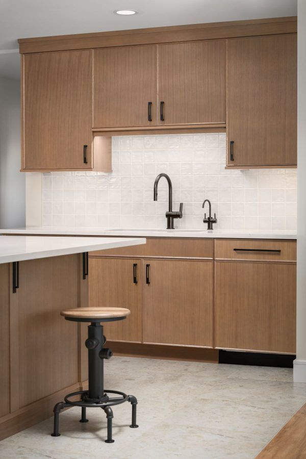 Modern kitchen with wood cabinets, white backsplash, black faucet, and a stool by the island.