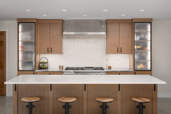 Modern kitchen with wood cabinets, white island, stainless range hood, and three stools