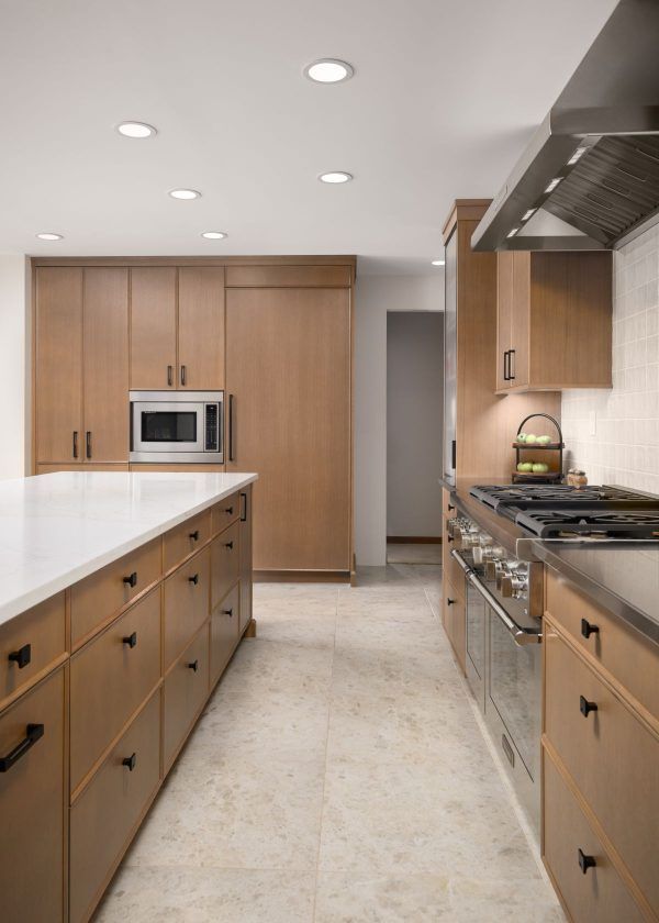 Modern galley kitchen with wood cabinets, white countertops, stainless appliances, and recessed lighting