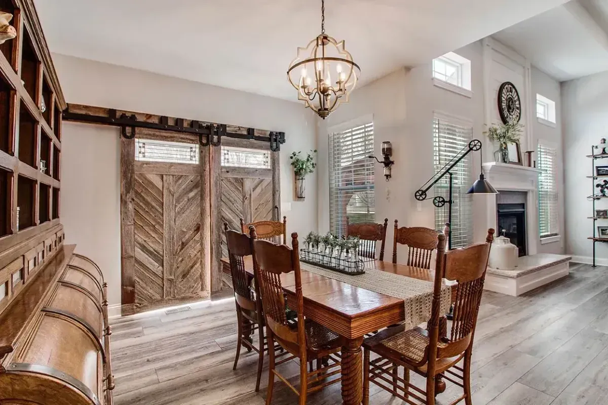 Bright dining room with rustic wood table, wicker chairs, chandelier, and barn-style doors