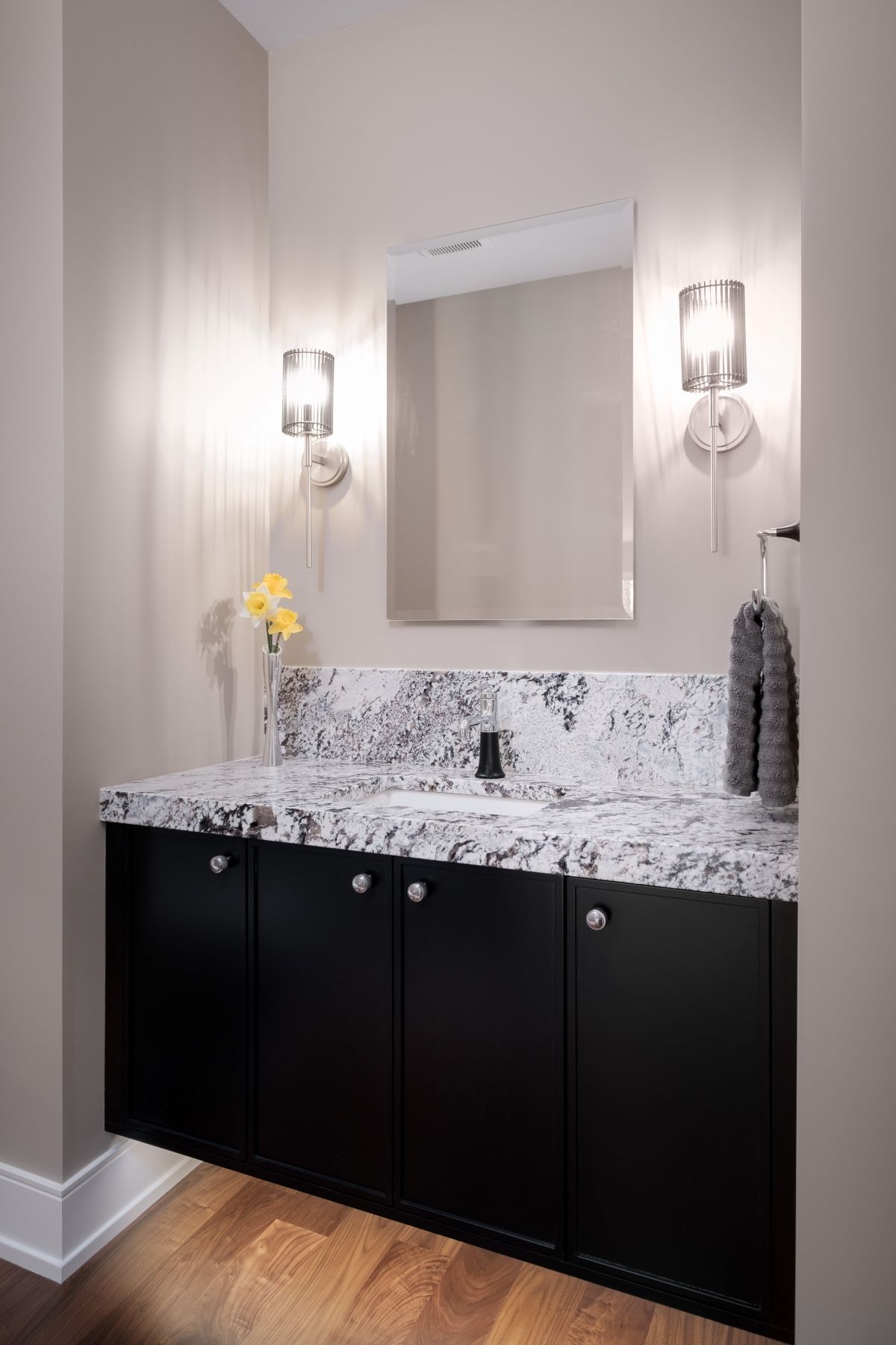 Modern bathroom vanity with black cabinets, marble countertop, mirror, and wall sconces