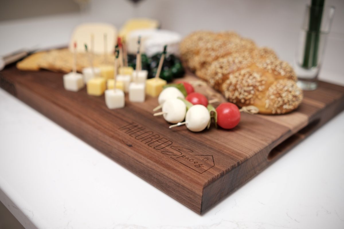 Cheese platter with bread, grapes, tomatoes, and small jars on a wooden board