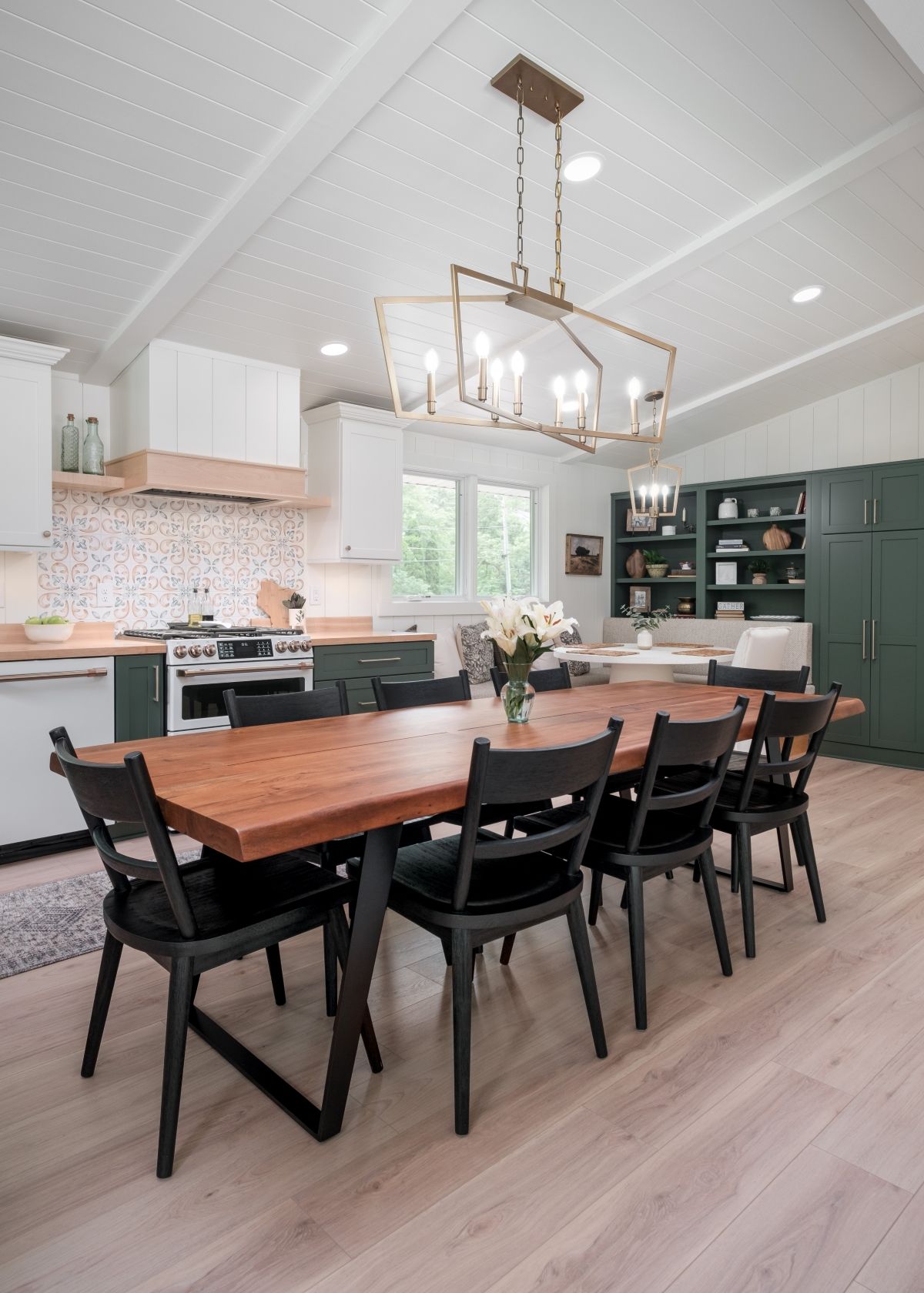 Modern kitchen-dining room with a wooden table, black chairs, pendant light, and green cabinets