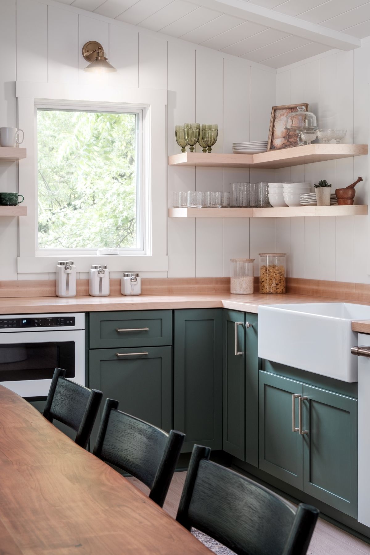 Modern kitchen with dark green cabinets, white walls, wooden countertops, and open shelves by a window