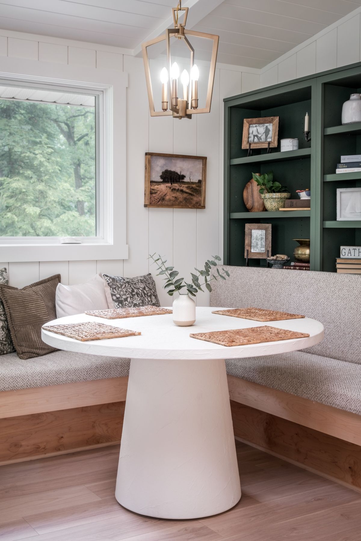 Cozy corner nook with white round table, built-in bench seating, green shelves, and a hanging pendant light