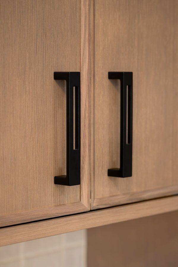 Close-up of two black handles on a light wood cabinet door.