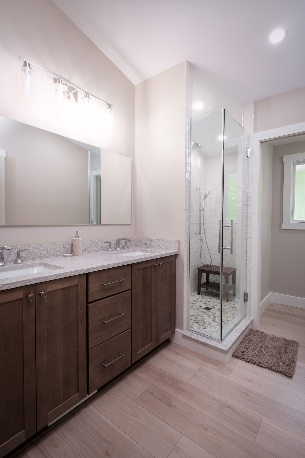 Modern bathroom with dark wood vanity, large mirror, glass shower, and light tile flooring.