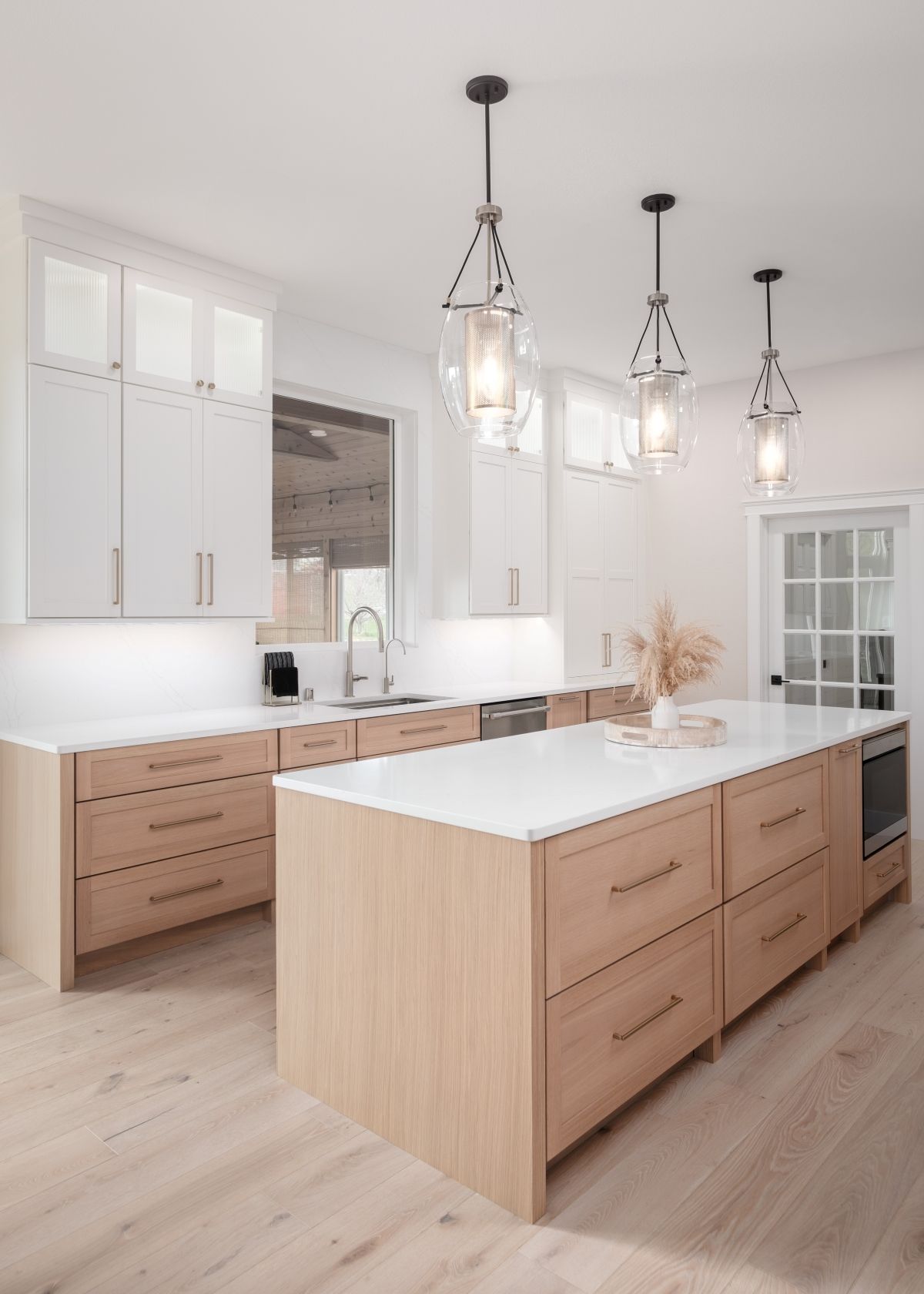 Bright modern kitchen with light wood island, white cabinets, and hanging glass pendant lights