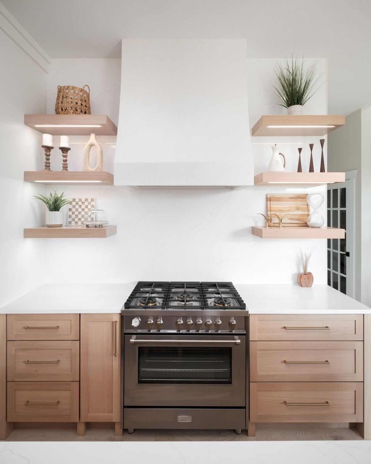 Modern kitchen with white walls, wood cabinets, floating shelves, and a black stove centered below a range hood