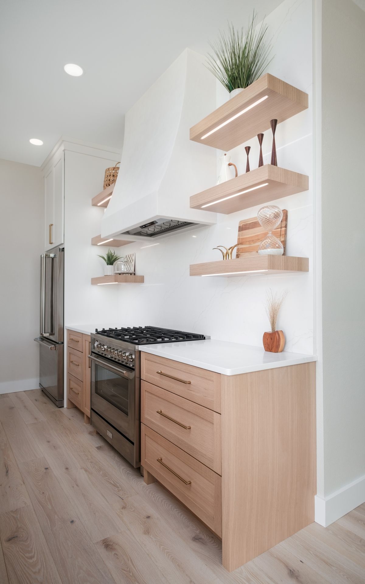 Bright modern kitchen with white walls, wood cabinets, stainless appliances, and floating shelves