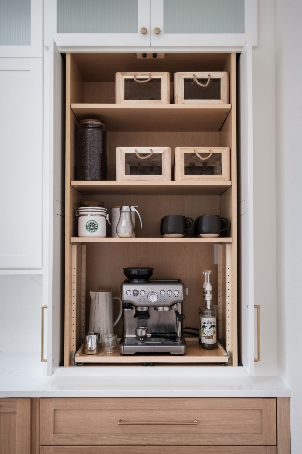 Built-in kitchen coffee nook with espresso machine, mugs, and storage bins on shelves
