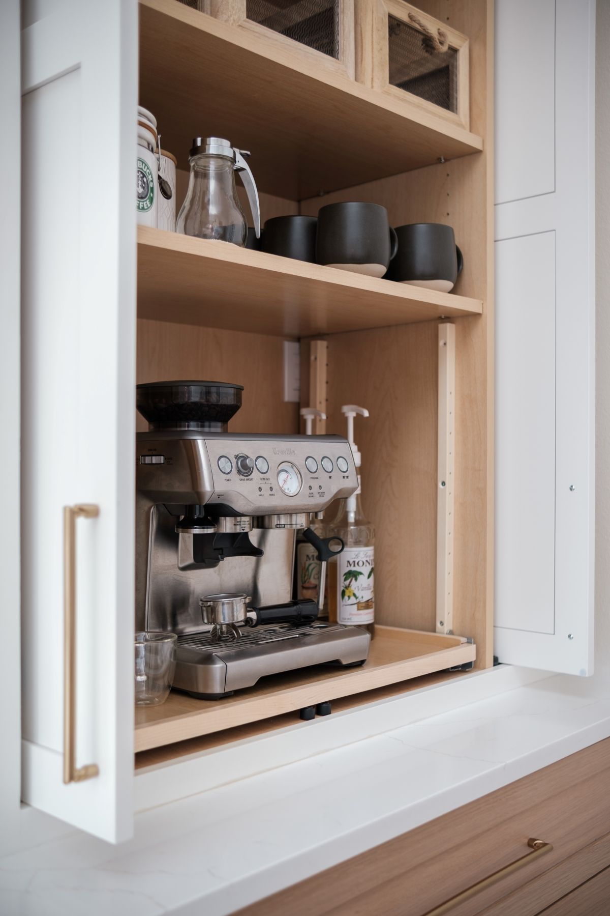 Built-in kitchen nook with a silver espresso machine, mugs, and cups on wooden shelves