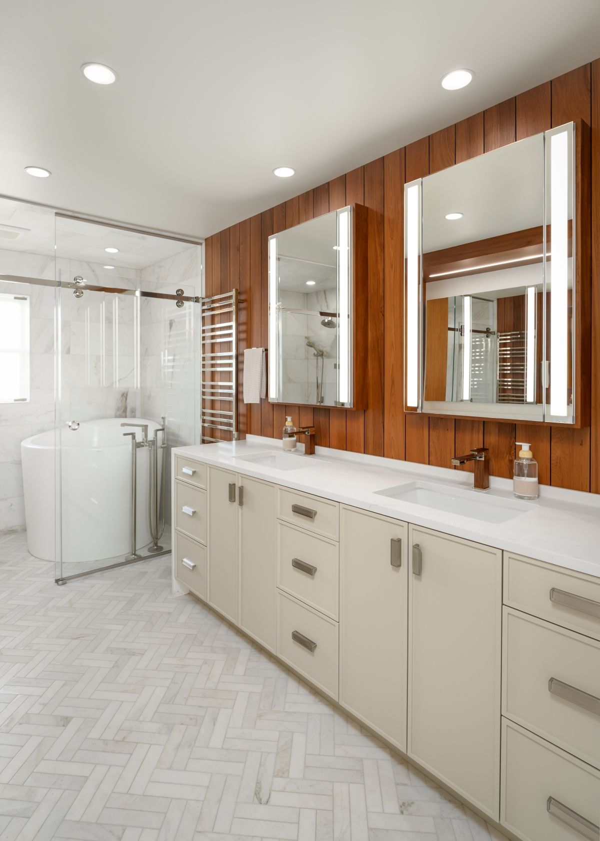Bright bathroom with double sinks, large mirrors, wood accent wall, and a glass shower.