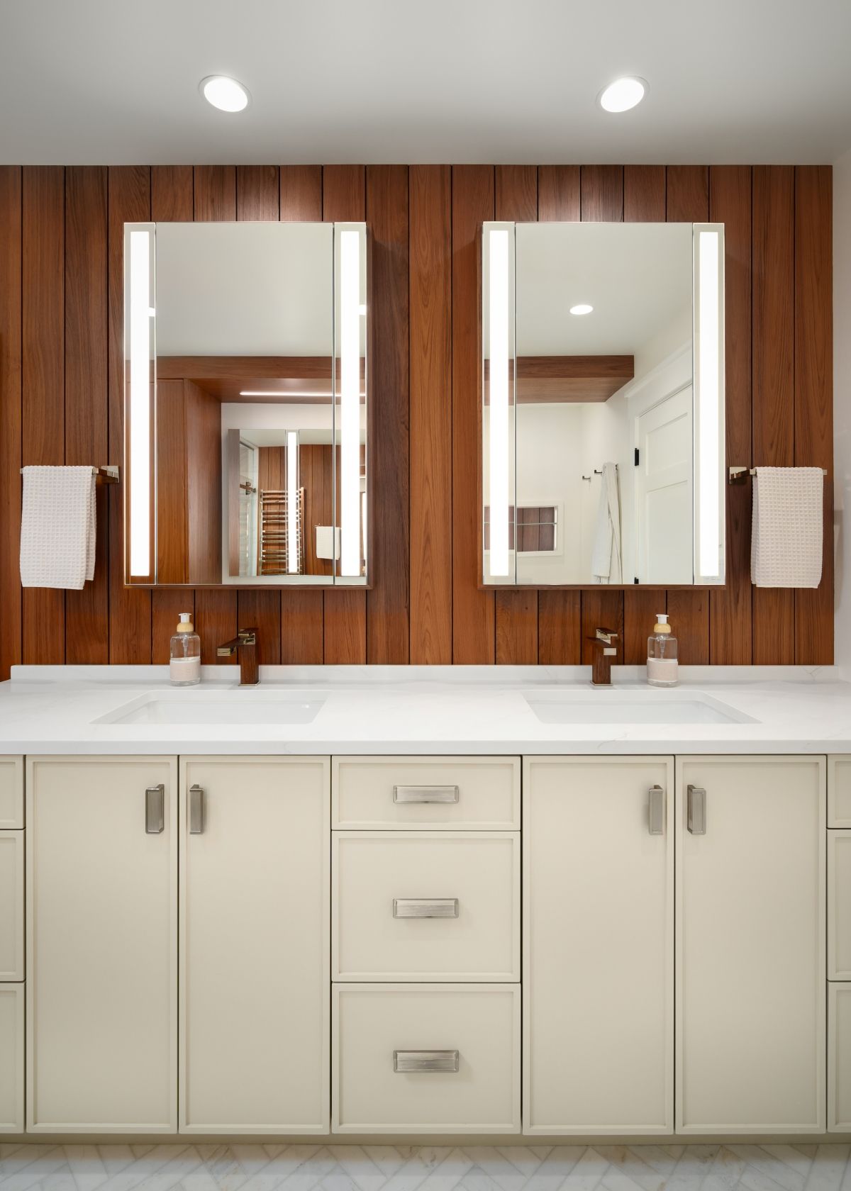 Modern bathroom vanity with double mirrors, wood-paneled wall, white cabinets, and sinks