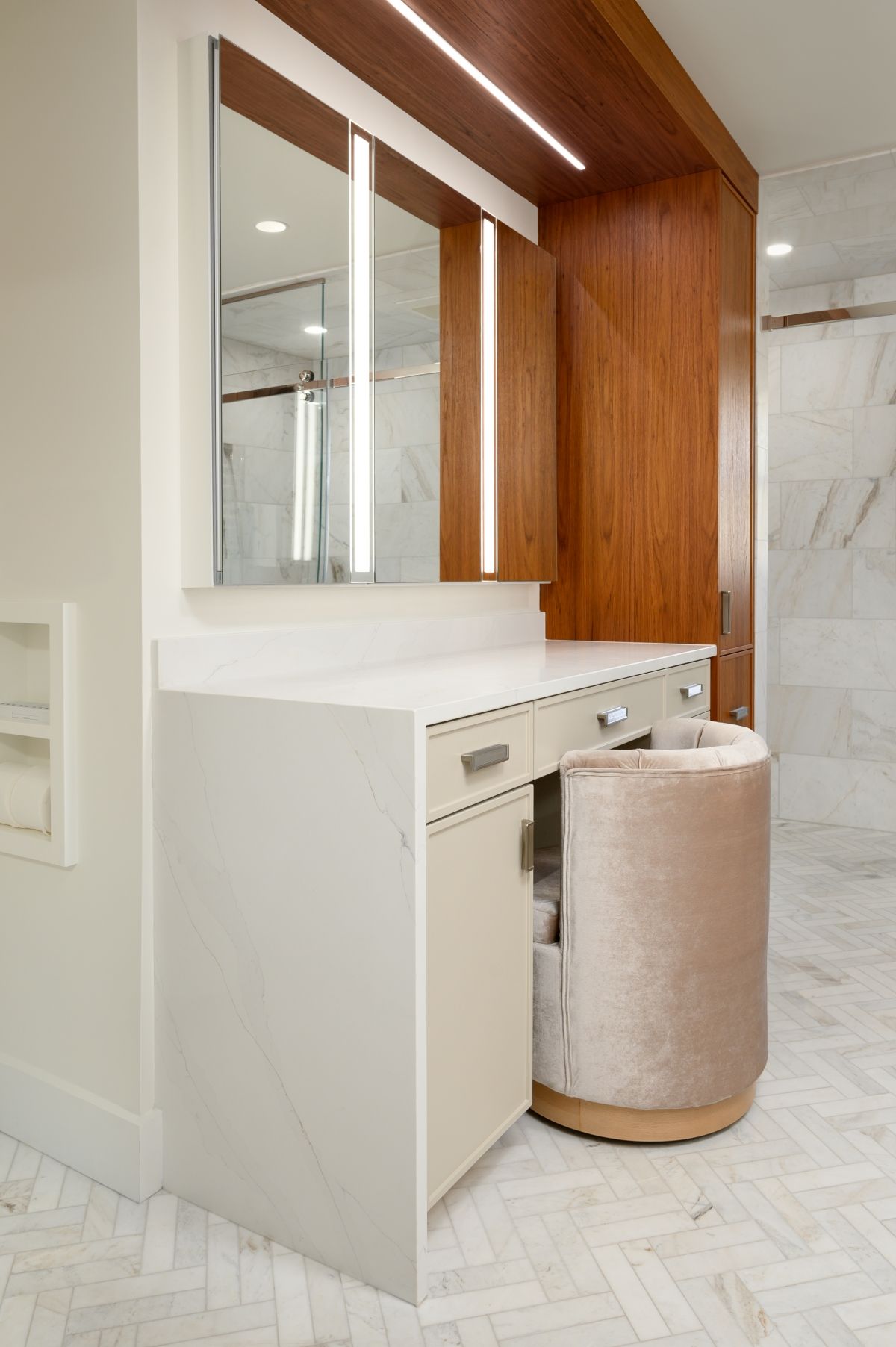 Modern bathroom vanity with white countertop, mirrored cabinets, wood paneling, and a round beige stool