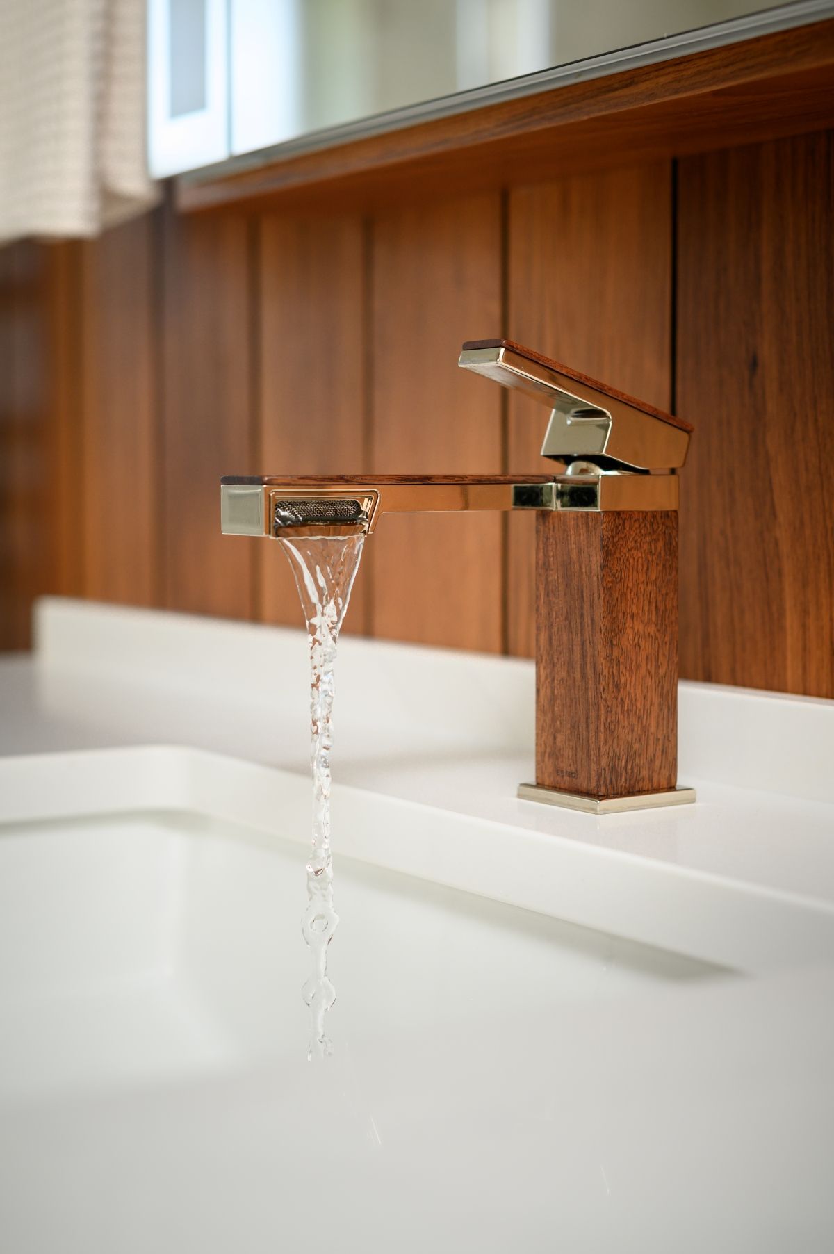 Modern wooden bathroom faucet running into a white sink basin