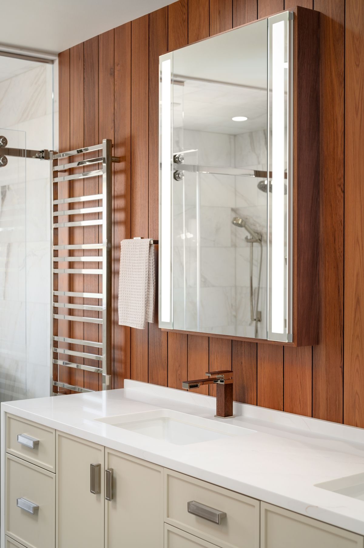 Modern bathroom with wood wall paneling, mirrored cabinet, vanity sink, and chrome towel warmer.