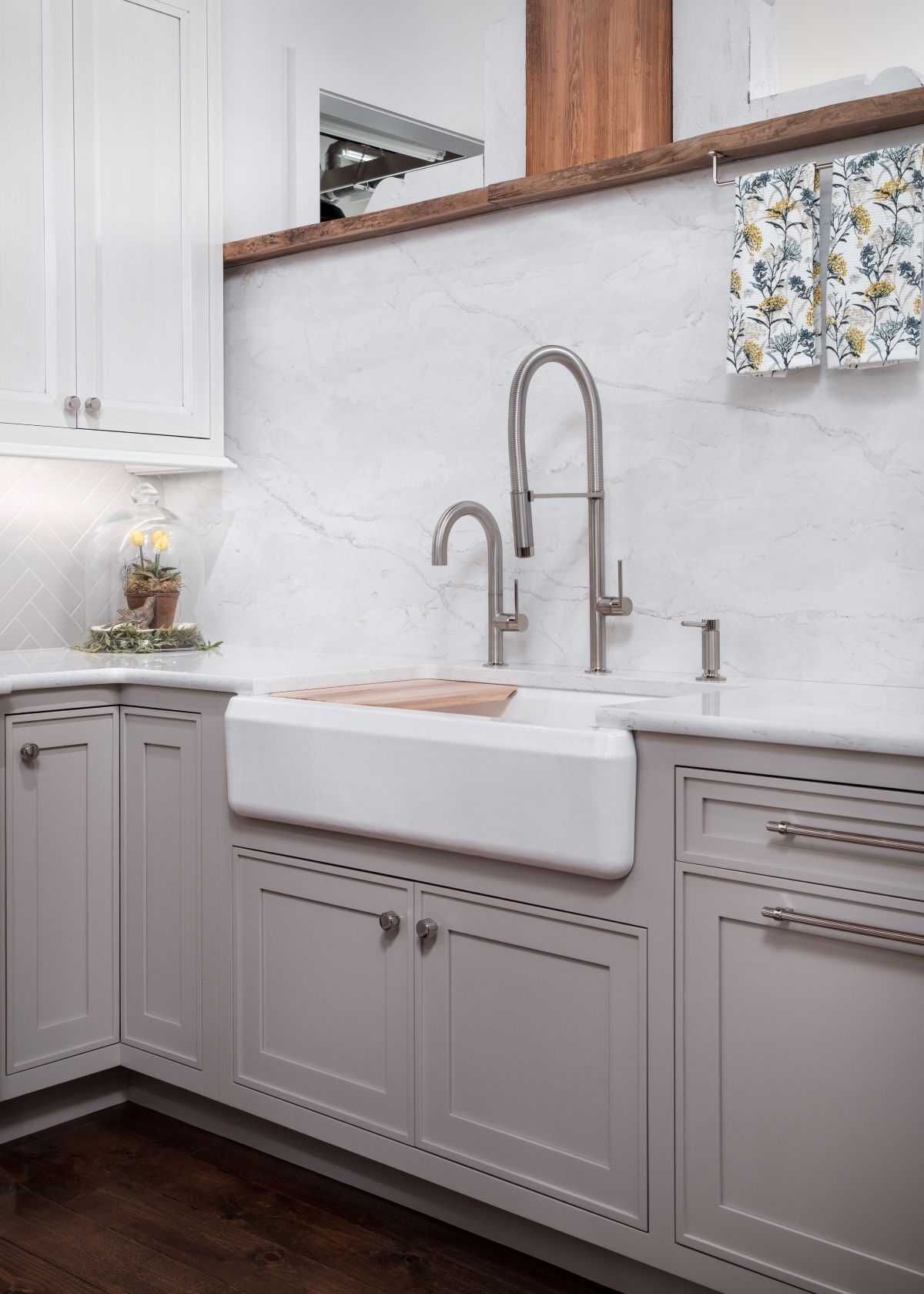 Bright white kitchen sink with tall faucet, marble backsplash, and gray cabinets under a wood shelf.