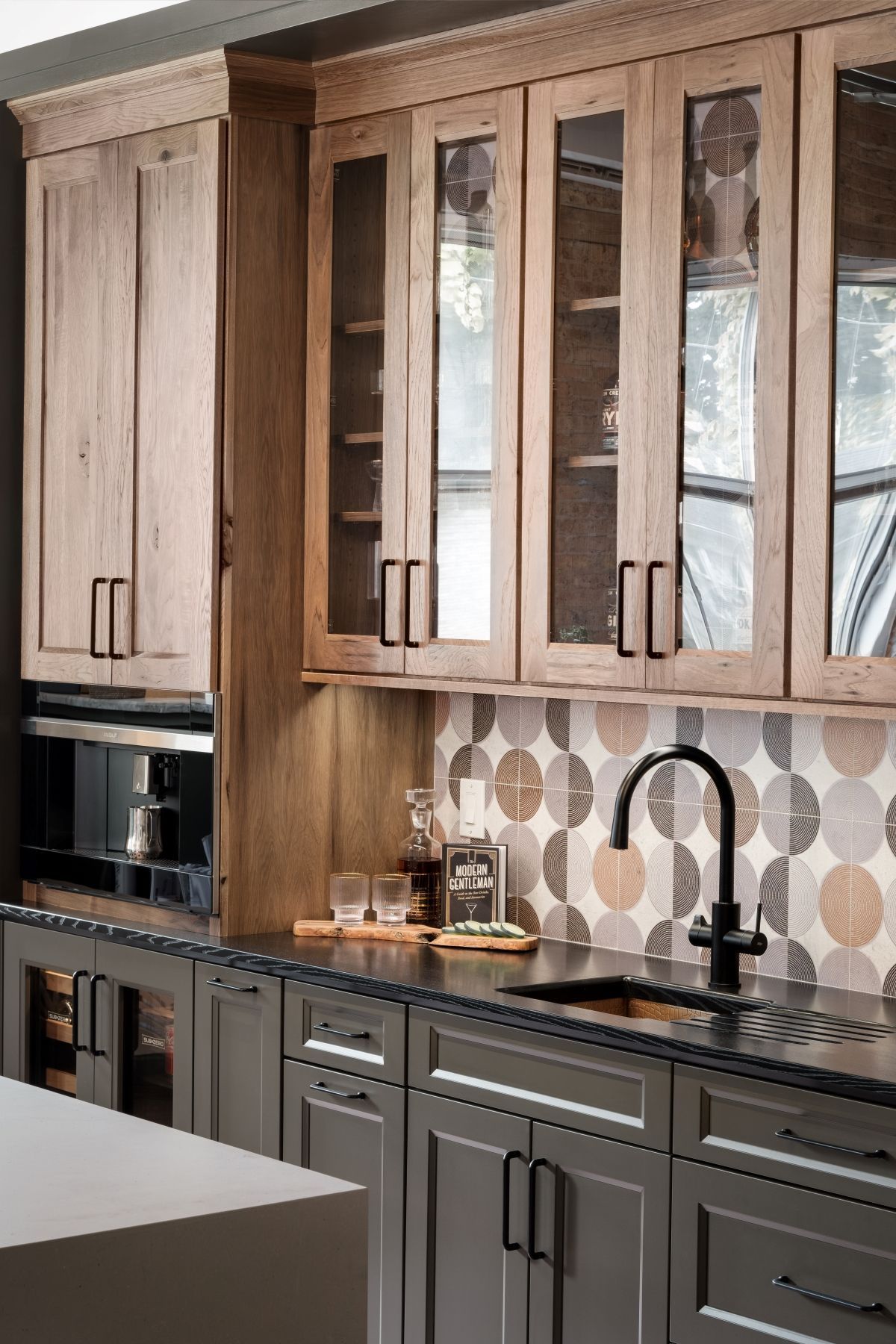Modern kitchen with wood cabinets, gray lower cabinets, a patterned backsplash, and a black faucet