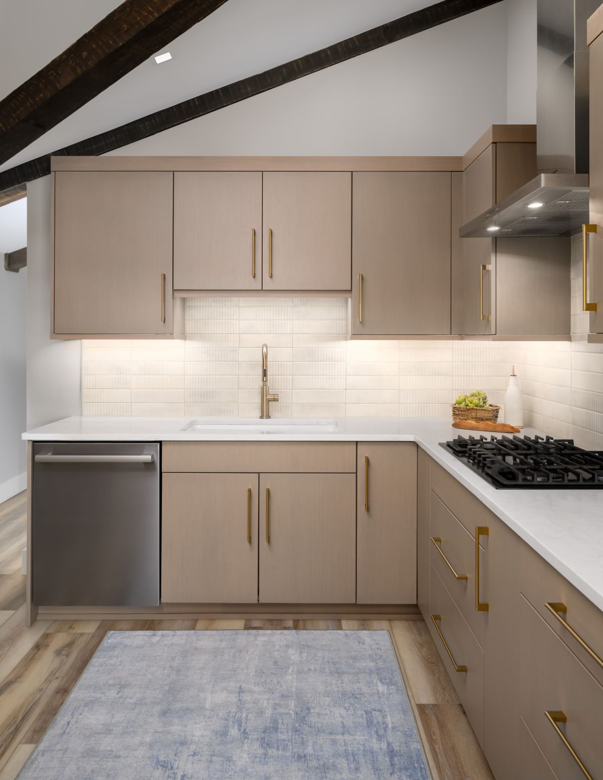 Modern kitchen with beige cabinets, white backsplash, stainless dishwasher, and a gas stove under a sloped ceiling.