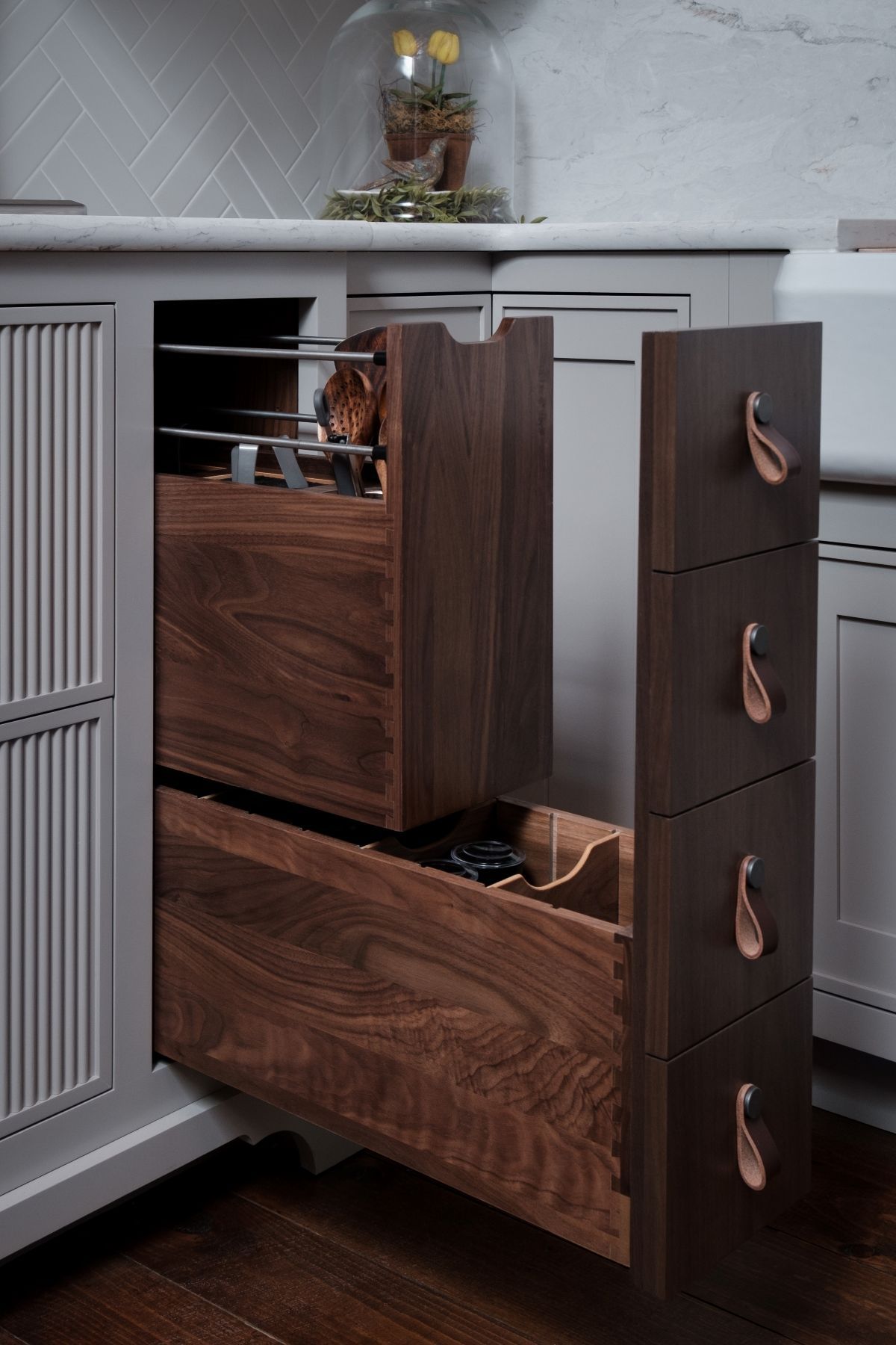 Wood and gray pull-out kitchen storage unit with drawers open, beside a cabinet in a modern kitchen.