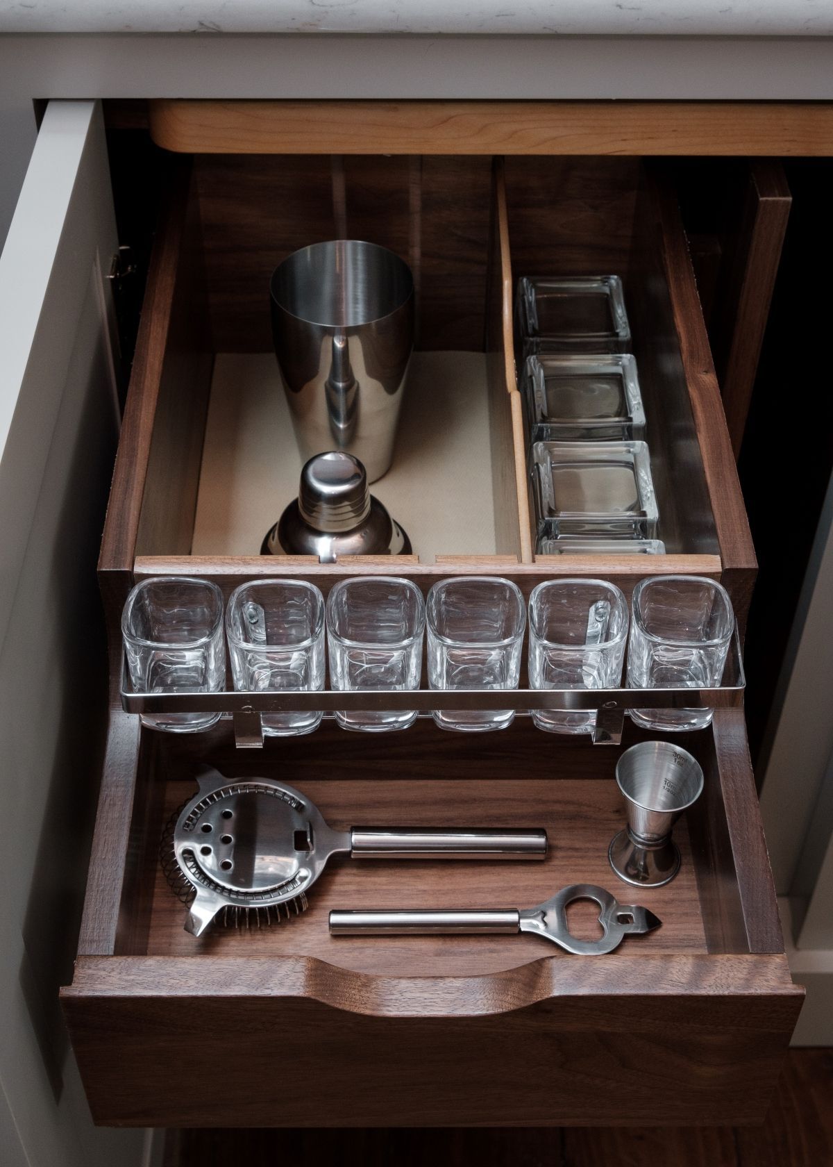 Drawer with cocktail tools and glassware, including a shaker, jigger, strainer, and ice tray.