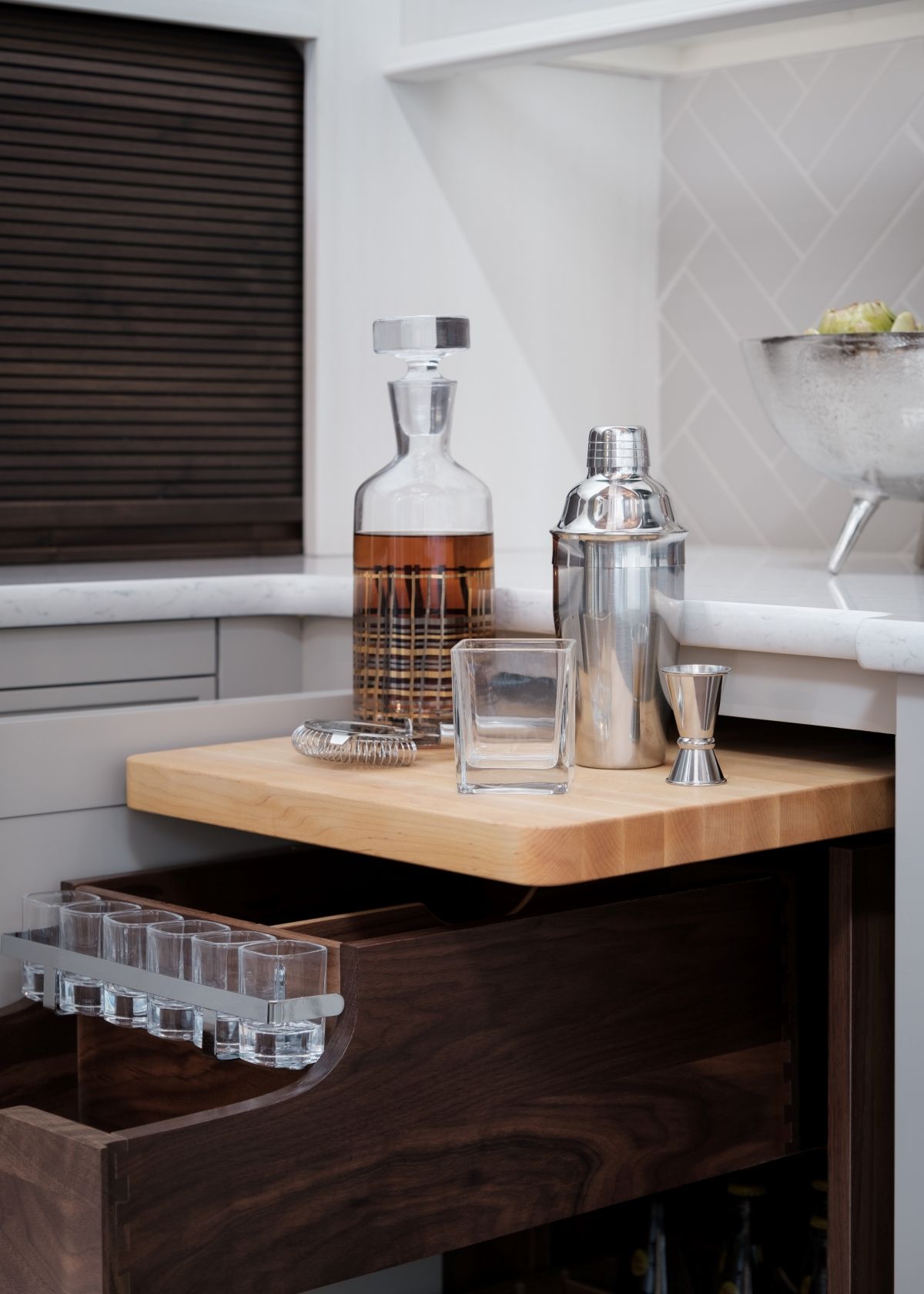 Tray with a decanter, cocktail shaker, and glass on a wooden bar cart in a modern room