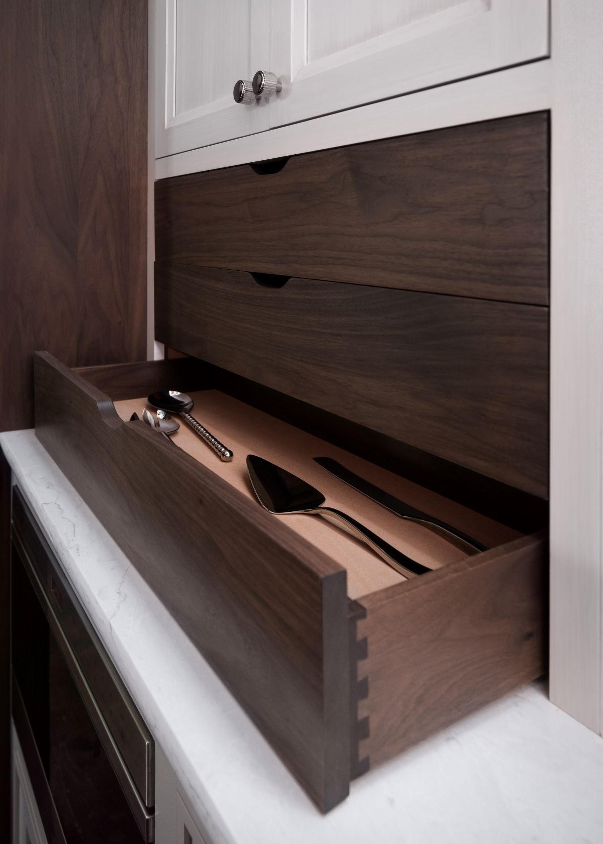 Partially open wooden drawer with sunglasses in a white cabinet.
