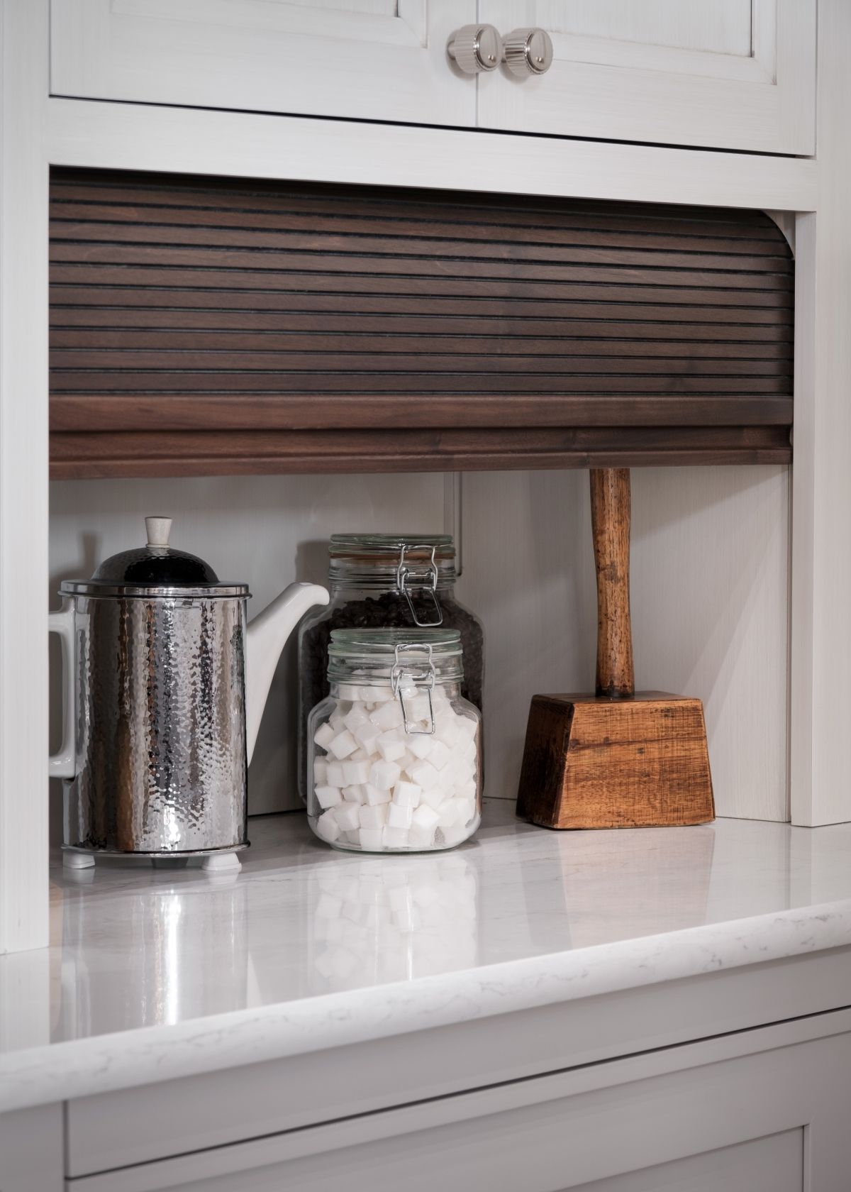 Kitchen shelf with jars and a silver canister under a dark brown shade, on a white countertop