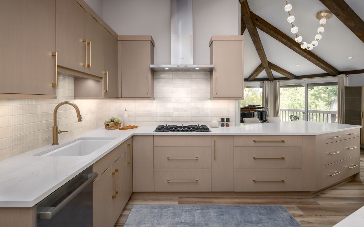 Modern beige kitchen with white countertops, gold fixtures, and vaulted wood-beam ceiling