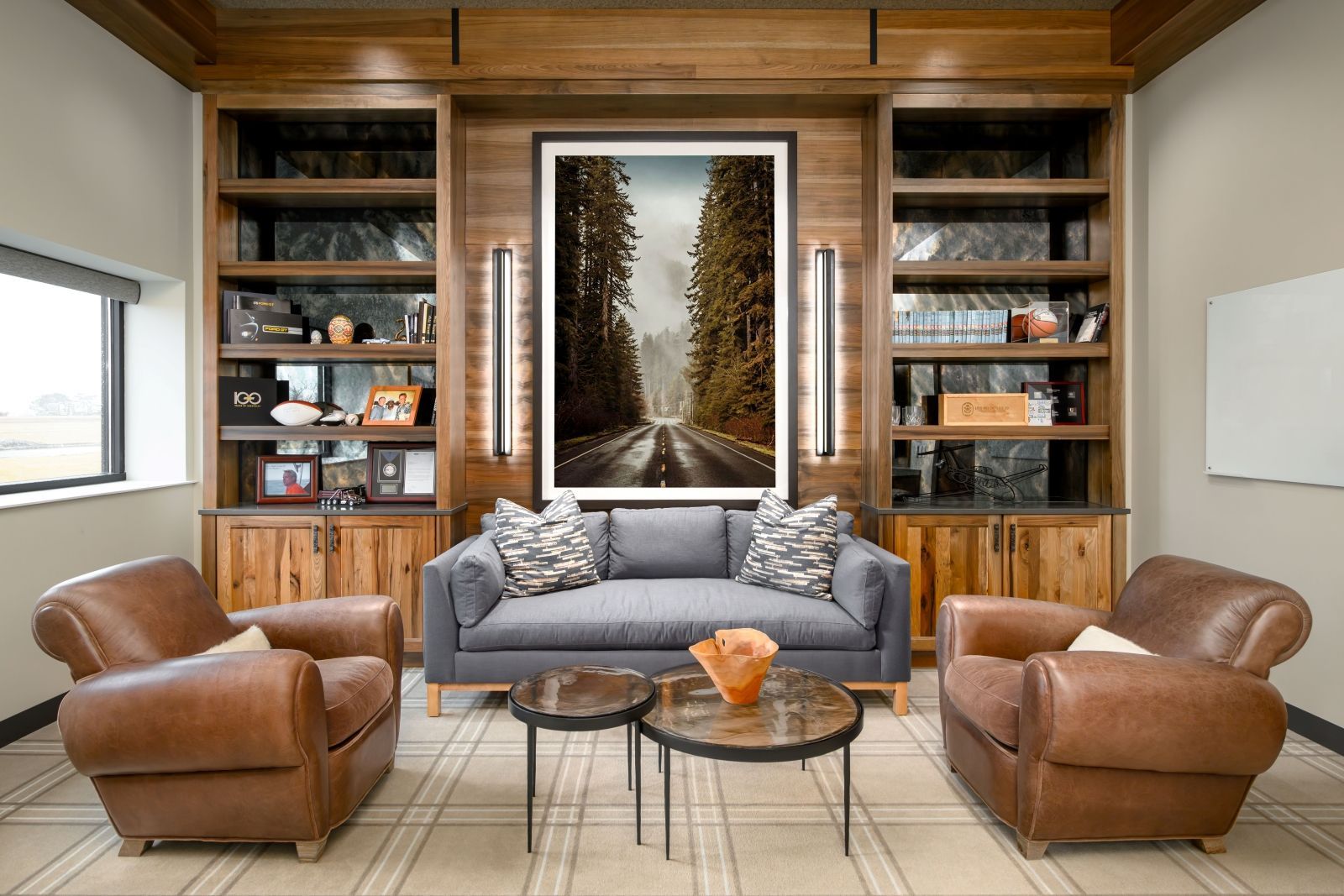 Modern living room with leather chairs, gray sofa, coffee table, and built-in bookshelves around a fireplace artwork