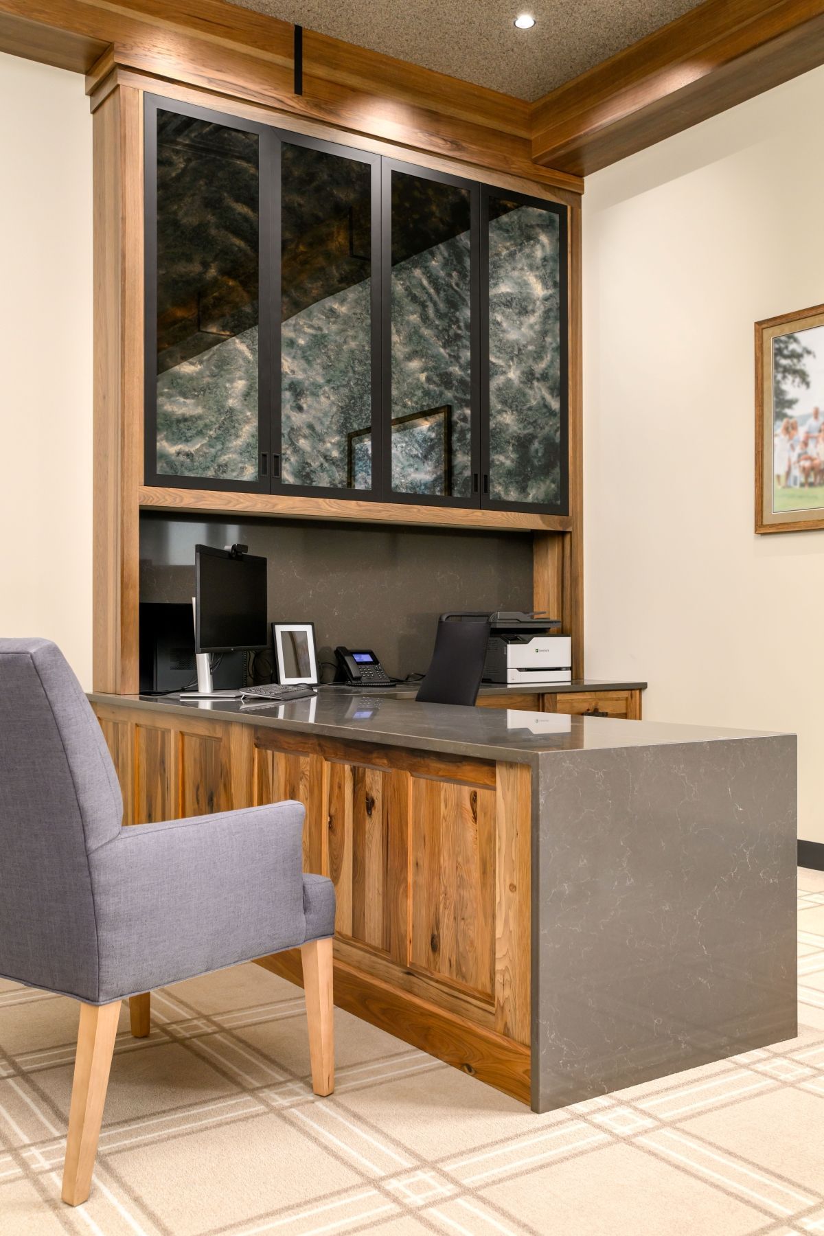 Office reception desk with gray chairs, wood paneling, and a large window overhead