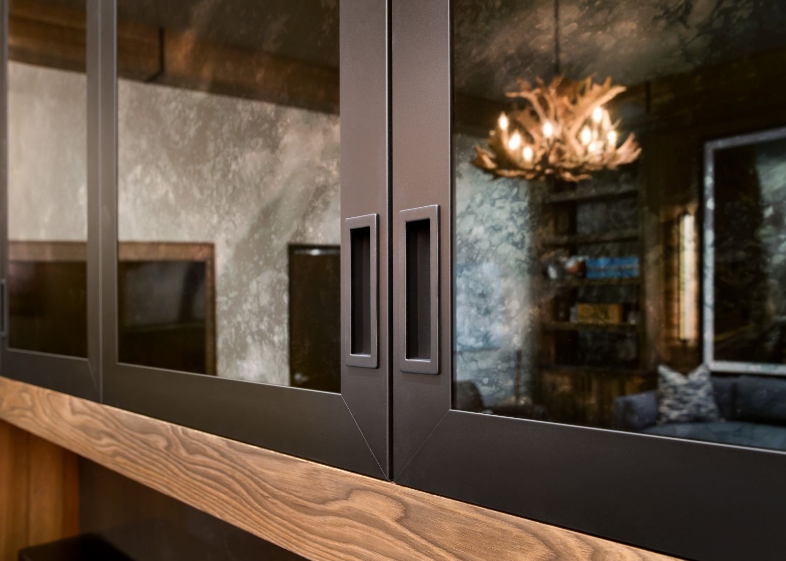 Dark cabinet doors with wood trim reflecting a chandelier in a room interior
