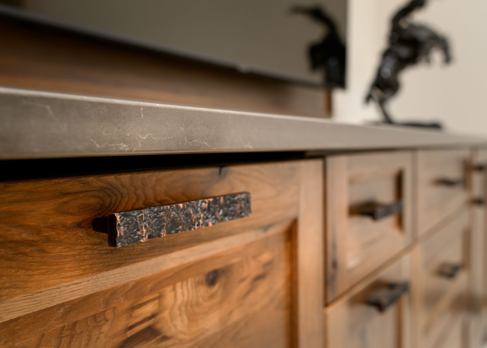 Wooden kitchen cabinet drawers with rustic metal pulls beneath a countertop