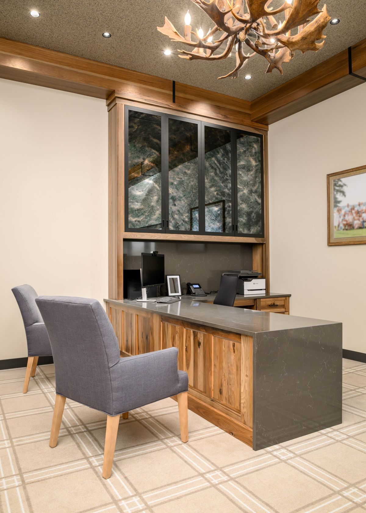Small modern office reception desk with two gray chairs, wood accents, and computer monitors