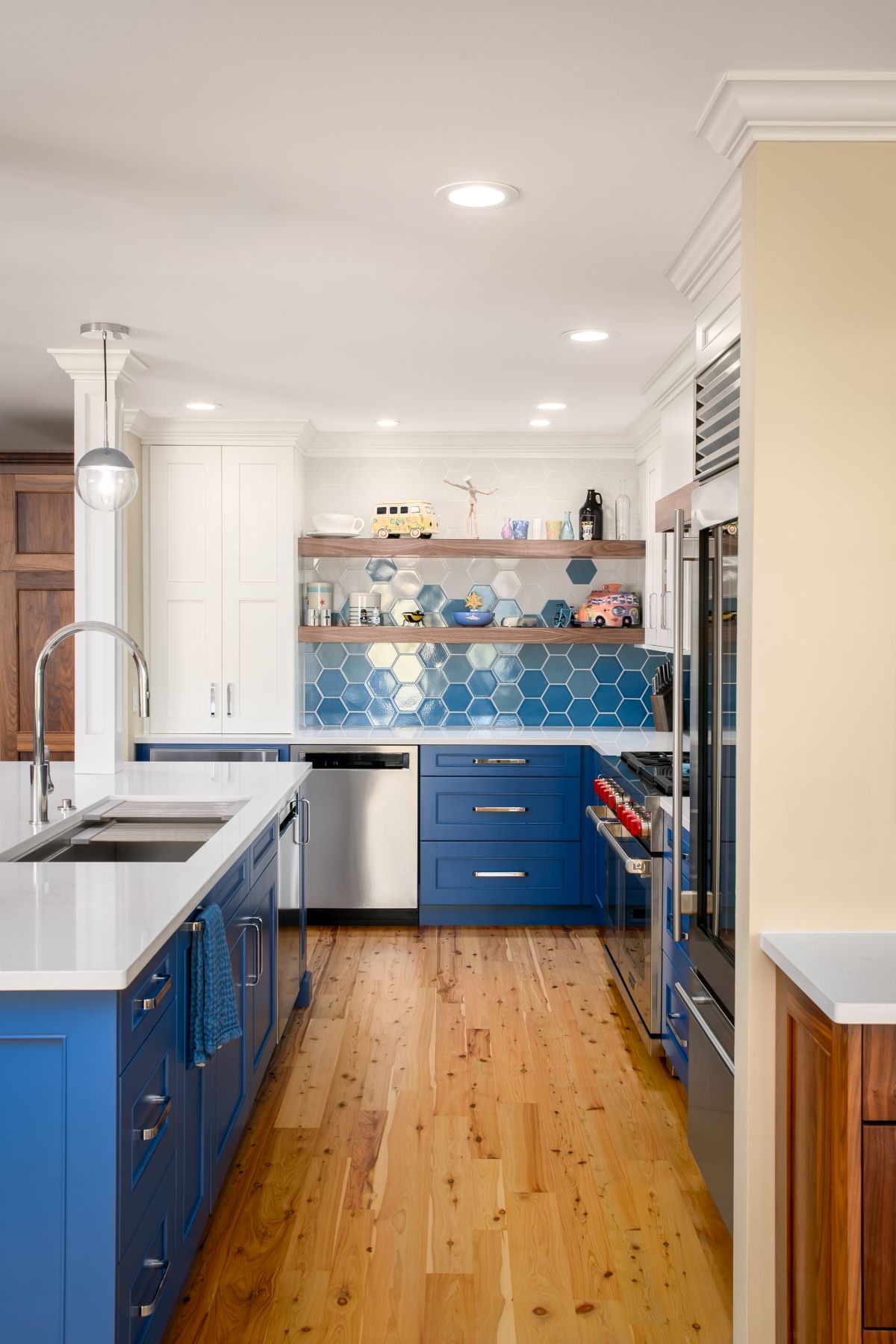 Bright blue-and-white kitchen with wood floors, stainless appliances, and open shelving.