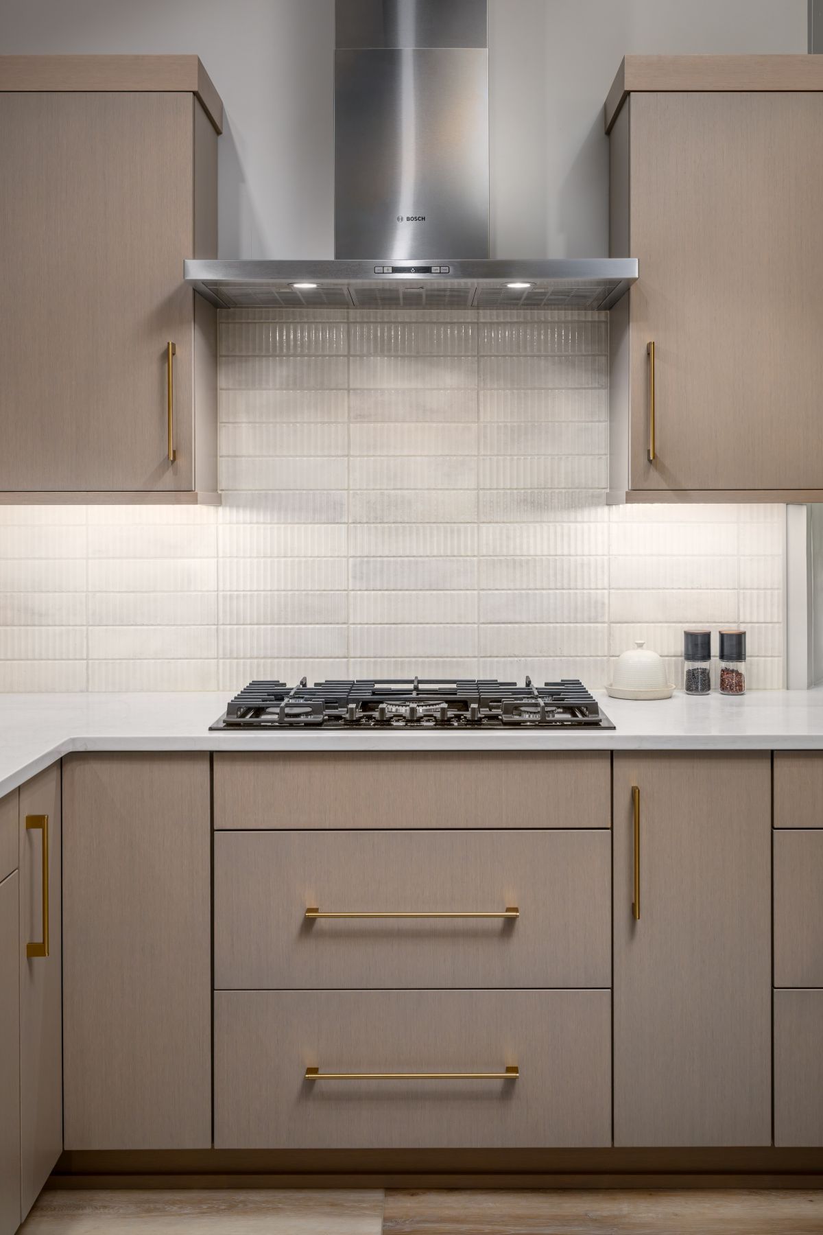 Modern kitchen with light wood cabinets, white tile backsplash, and stainless steel range hood over gas cooktop