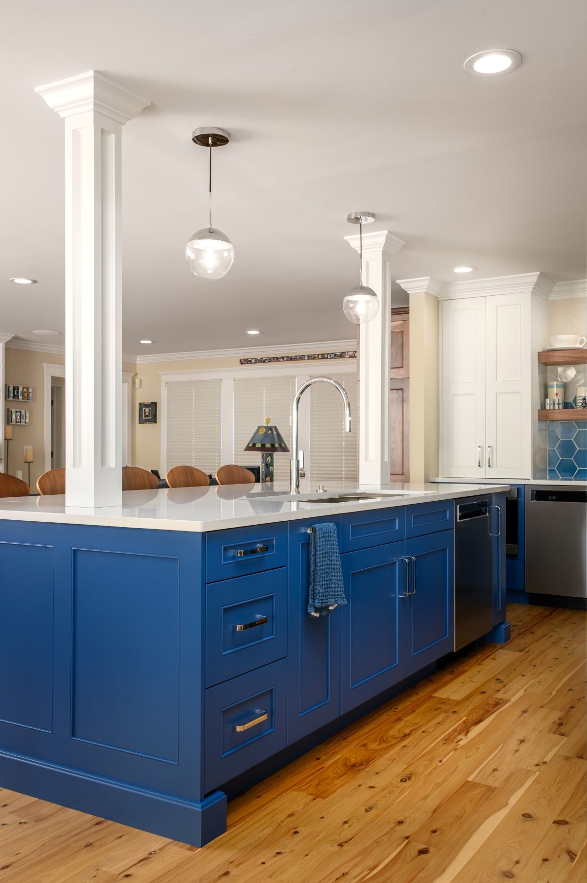 Bright blue kitchen island with white columns and hardwood floors in a modern open kitchen