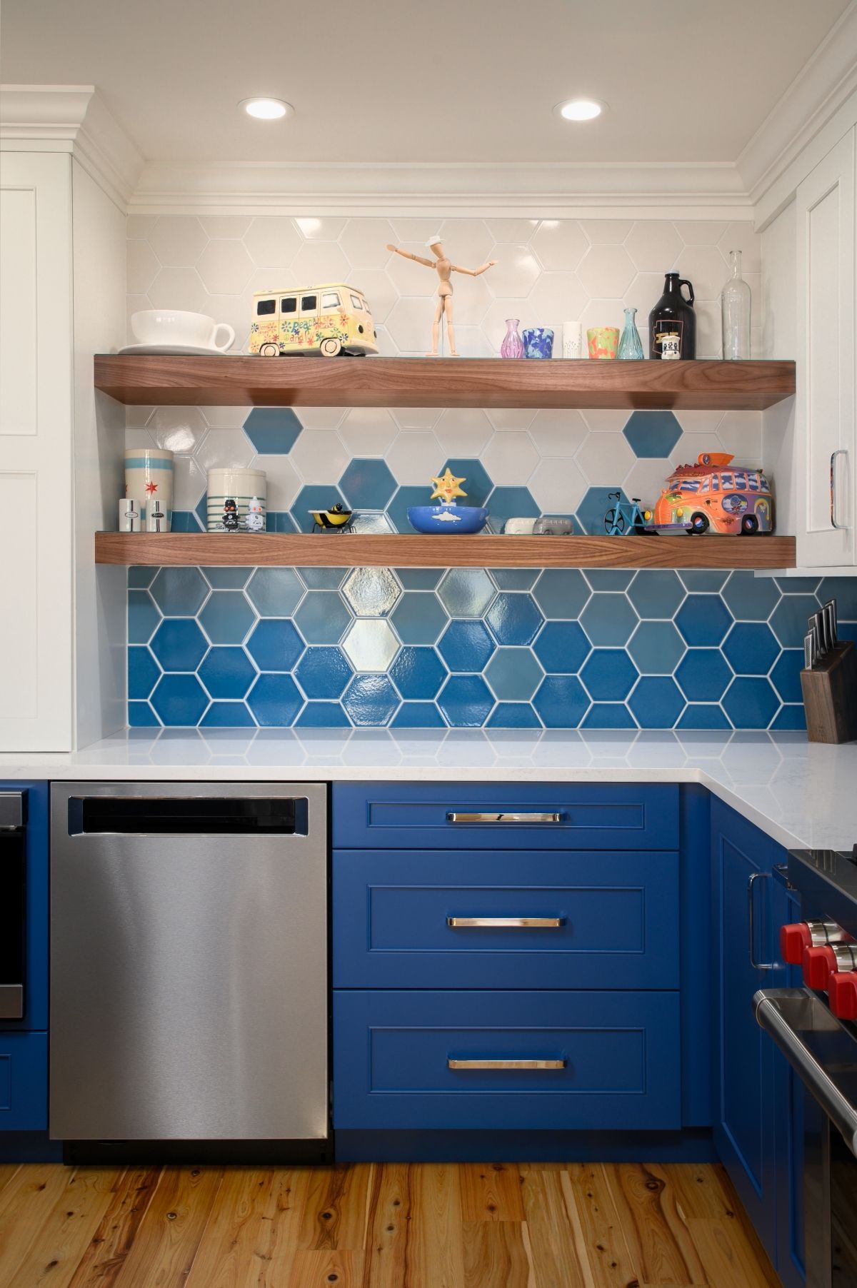 Blue kitchen nook with hexagon tile backsplash, wooden shelves, and a stainless dishwasher.